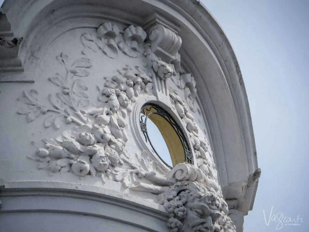 The top of a cement concrete statue, with floral details and a face cut off at the bottom. There is also a small glass circle in the center. 