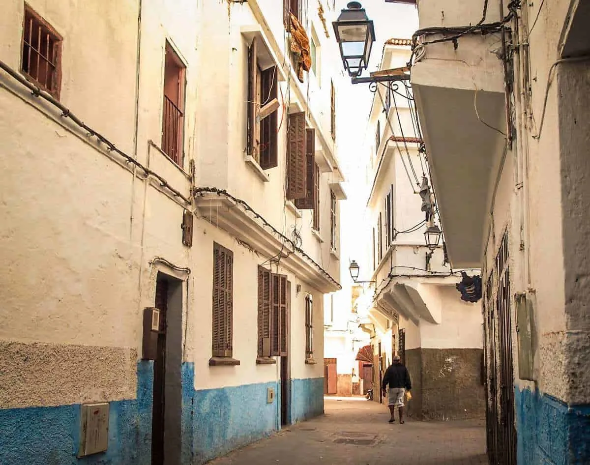 A man wandering down an empty street in Casablanca, Morocco with buildings that are blue on the bottom and white on top.