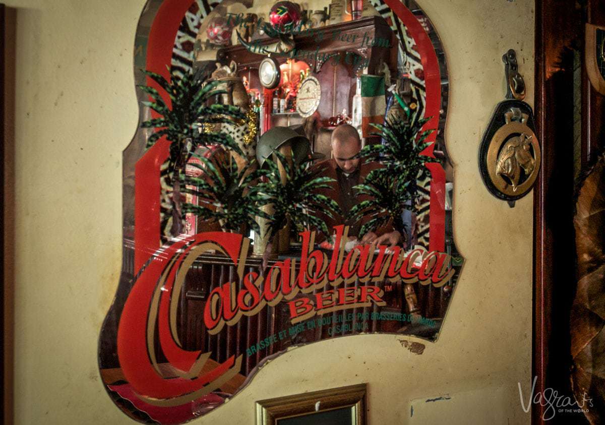 A mirror that says Casablanca Beer in red letters, with a bartender reflected in the mirror.
