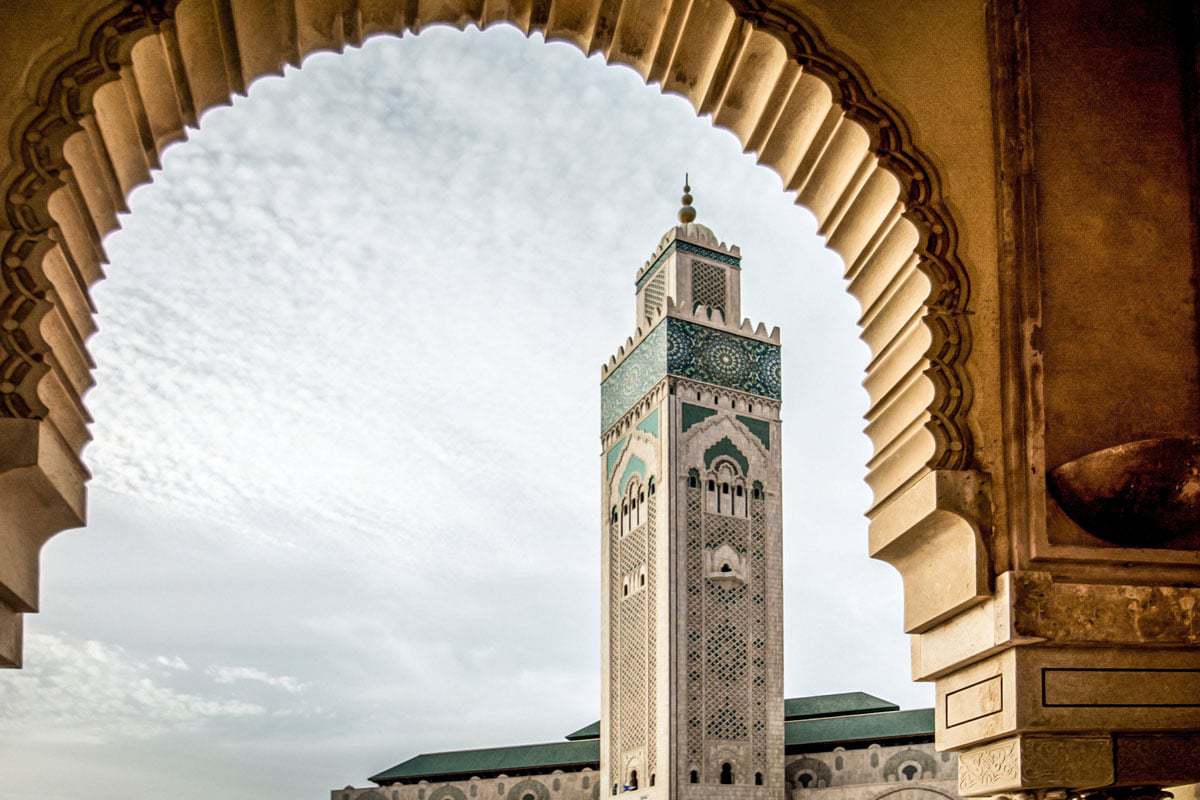 A view of the stunning Hassan II Mosque with green tiles through an arch.