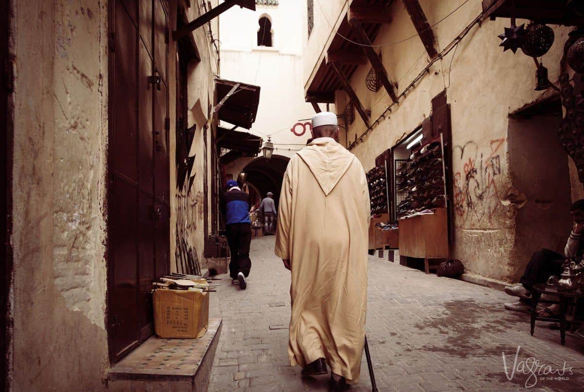 Man walking in the dark streets of Fez medina in conservative traditional dress.