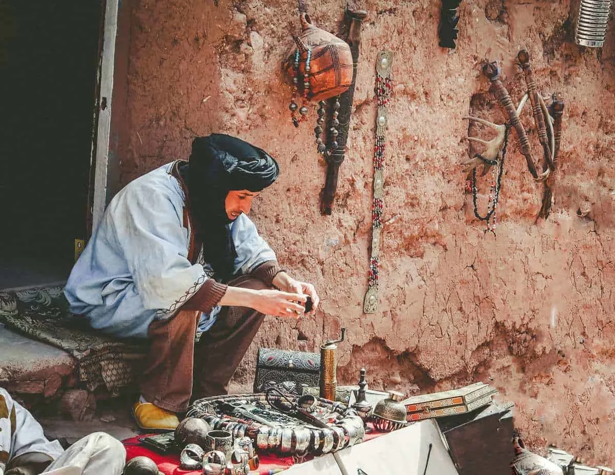 Seated Moroccan man making metal handicrafts in Ait Benhaddou Morocco. A great thing to see on a Moroccan Road Trip and to buy if you know how to haggle moroccan style.