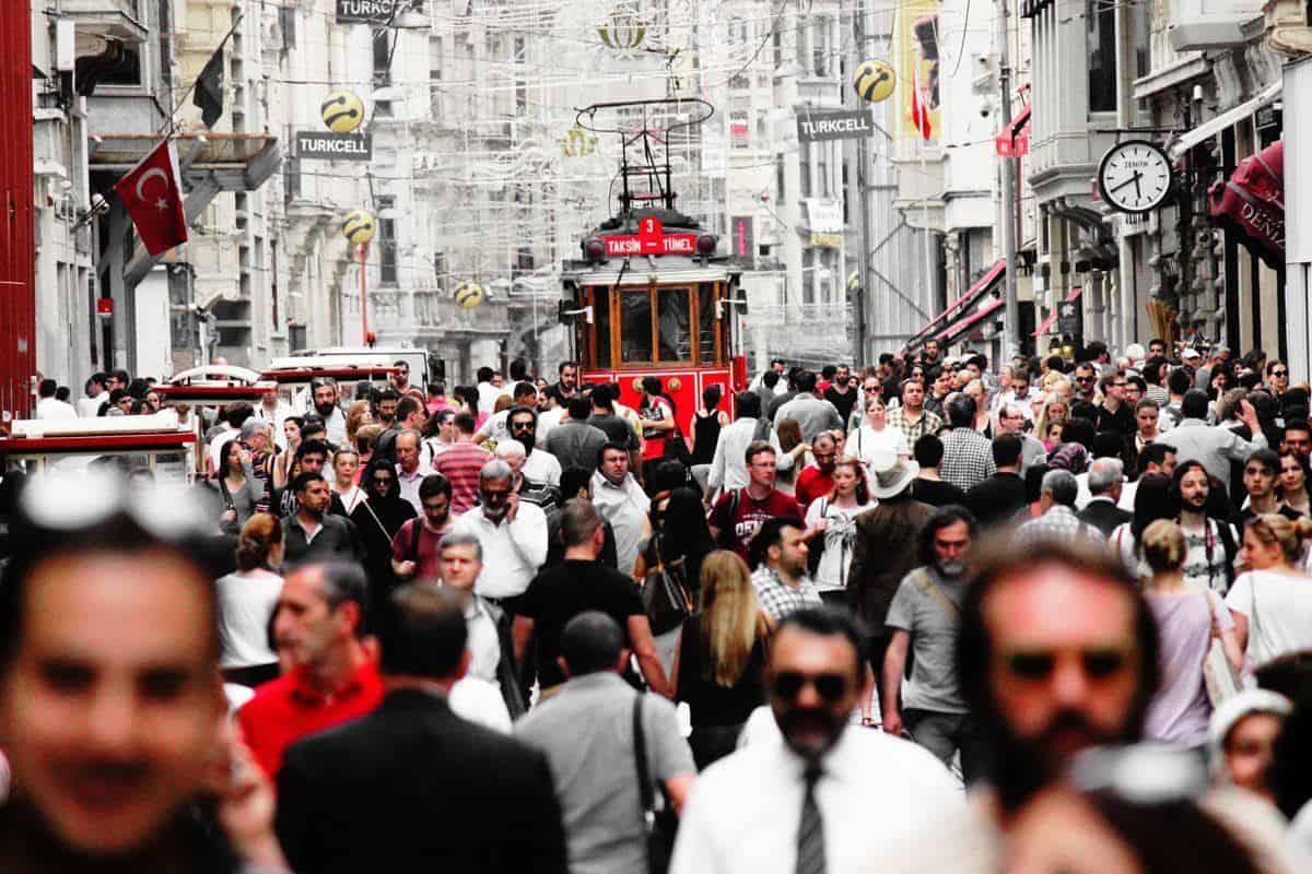 A crowded street with a red tram coming through a throng of people.