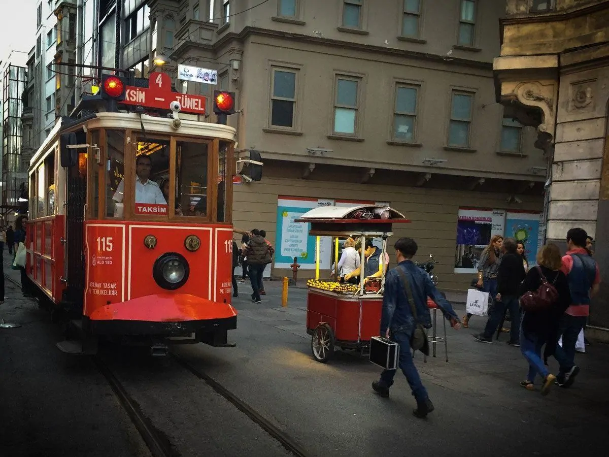 Famous red Istanbul tram coming past street stall cart selling chestnuts.