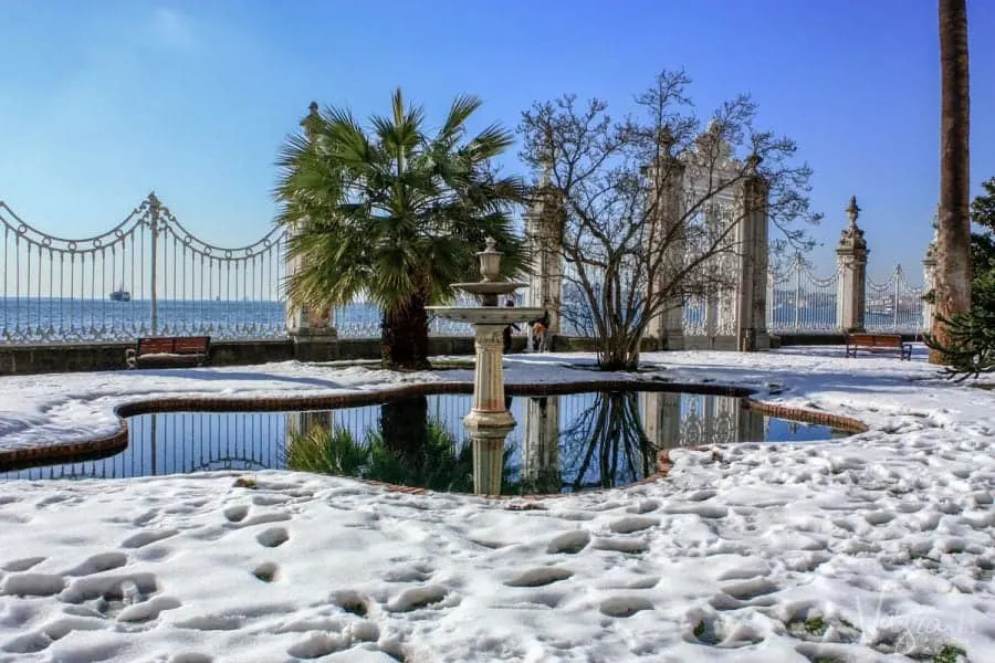Snow around small lake and fountain outside Dolmabahçe Palace with the Bosphorus in the distance.