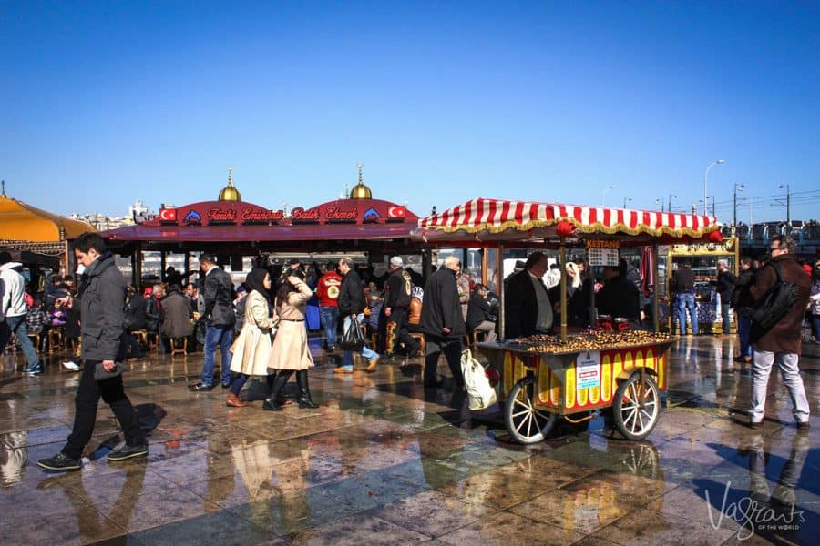 A man selling chestnuts from a colourful cart in a busy square in Istanbul. 