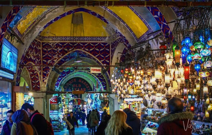 People walking into the Old Bazaar in Istanbul with hundreds of lanterns in a display next to the entry.