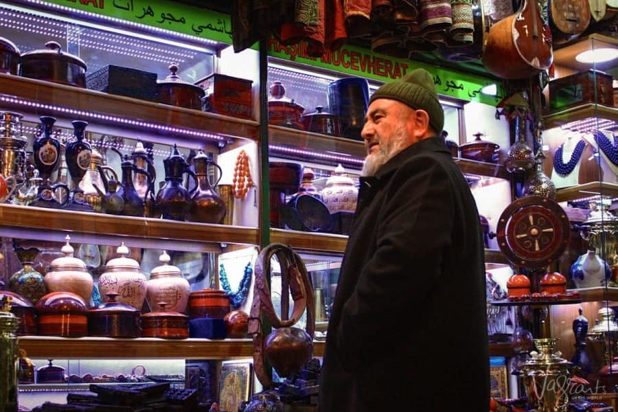 A Turkish man with a goatee beard wearing a heavy coat and a beanie selling vases in the the Bazaar Istanbul. 