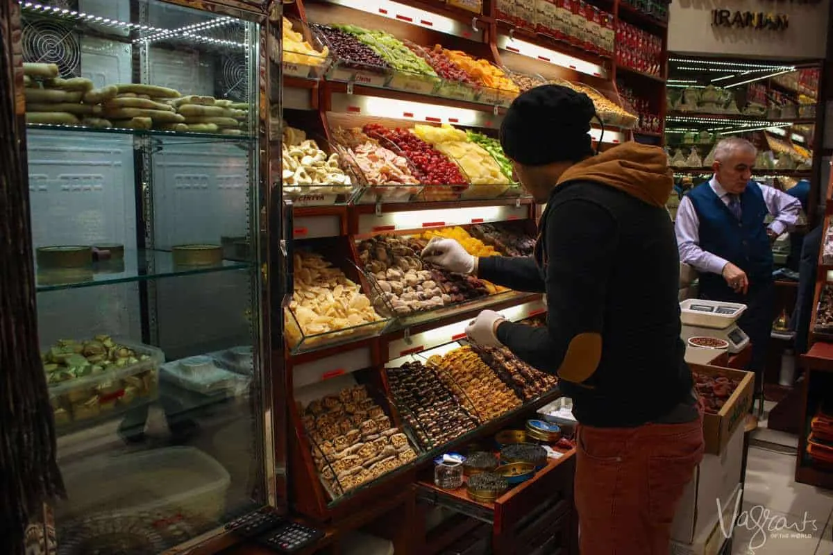 A young man places dates neatly on display next to lots of colourful dried fruits in the Spice Bazaar Istanbul