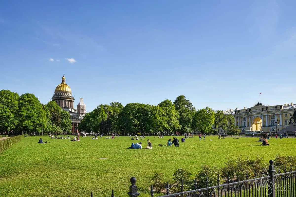 people sitting in a green park in summer in ST Petersburg with an iconic gold dome roof in the background. 