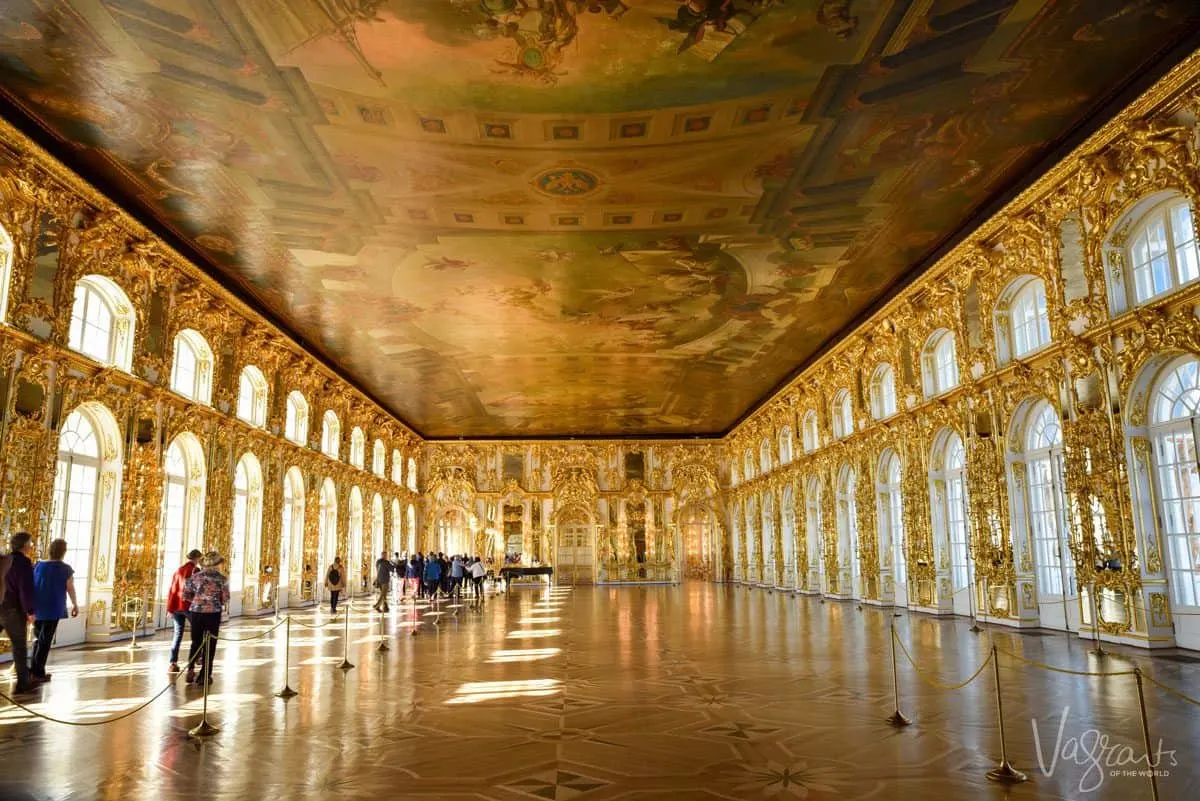 Golden room with light spilling through the archways and people looking at the painted ceilings and golden walls.  you will see these things in Russia if you go on a viking river cruise and cruise St Petersburg to Moscow