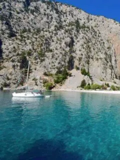 yacht moored in bay surrounded by crystal clear blue waters and steep cliffs. A perfect greek island for beaches, swimming and boating.