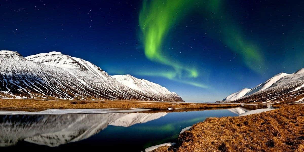 Green aurora over snow-capped mountains reflected in still water in Iceland
