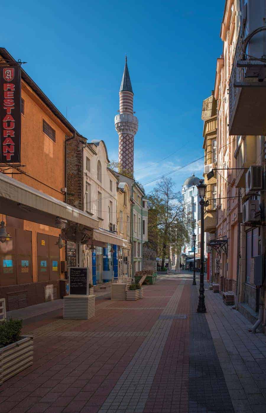 A pedestrian only street lined with shops and a mosque minaret at the end. 
