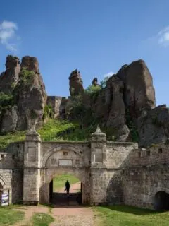 Person walking through the gates of Belogradchik Rocks Fortress on a blue sky day.
