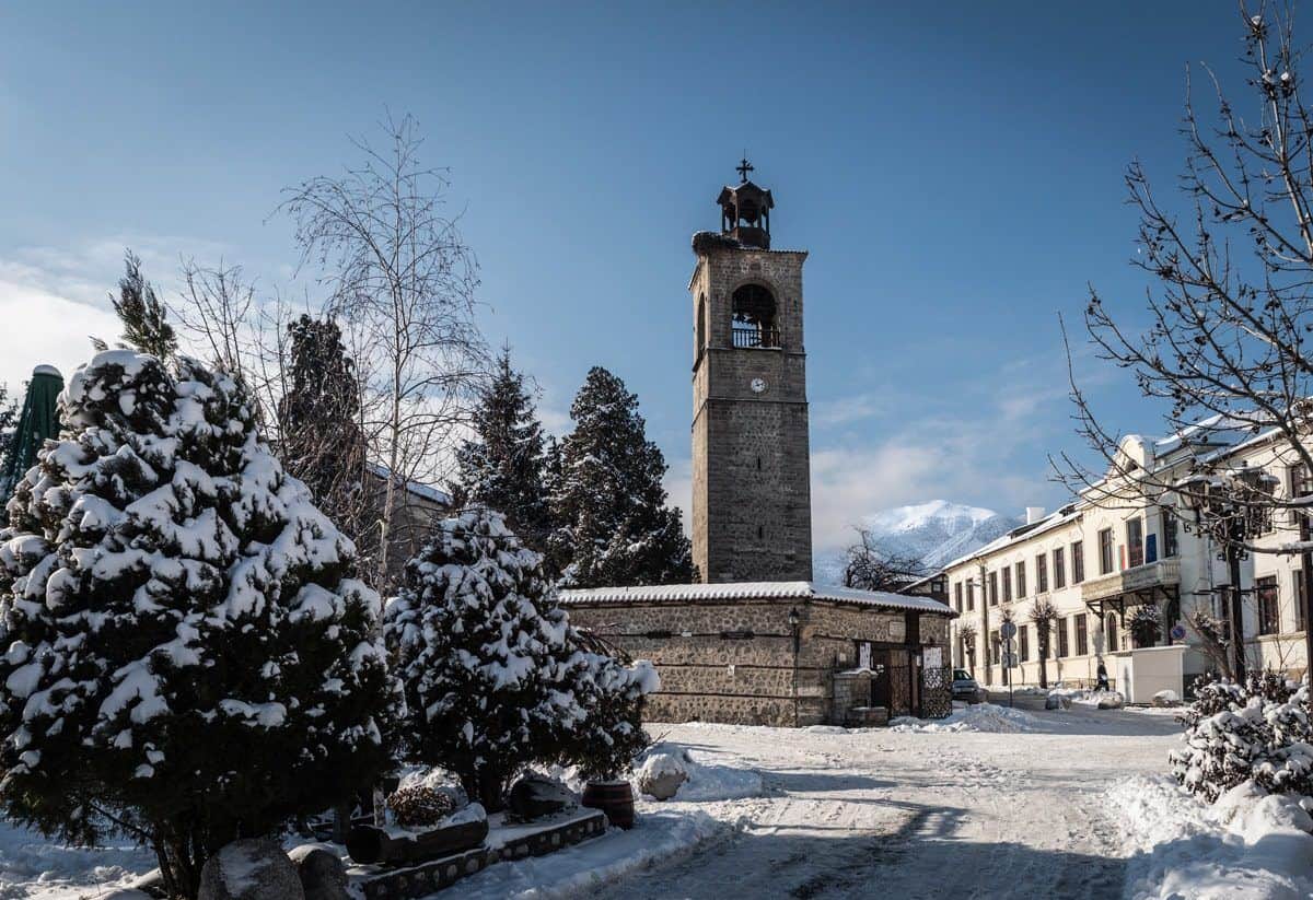 Snow-laden pines around the stone clock tower in Bansko town square