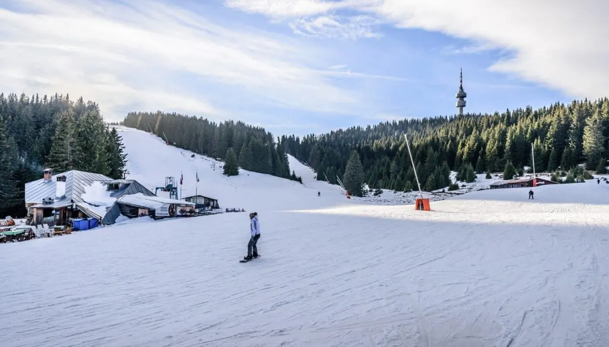 A snowboarder crossing a wide beginner slope below the Snezhanka tower at Pamporovo