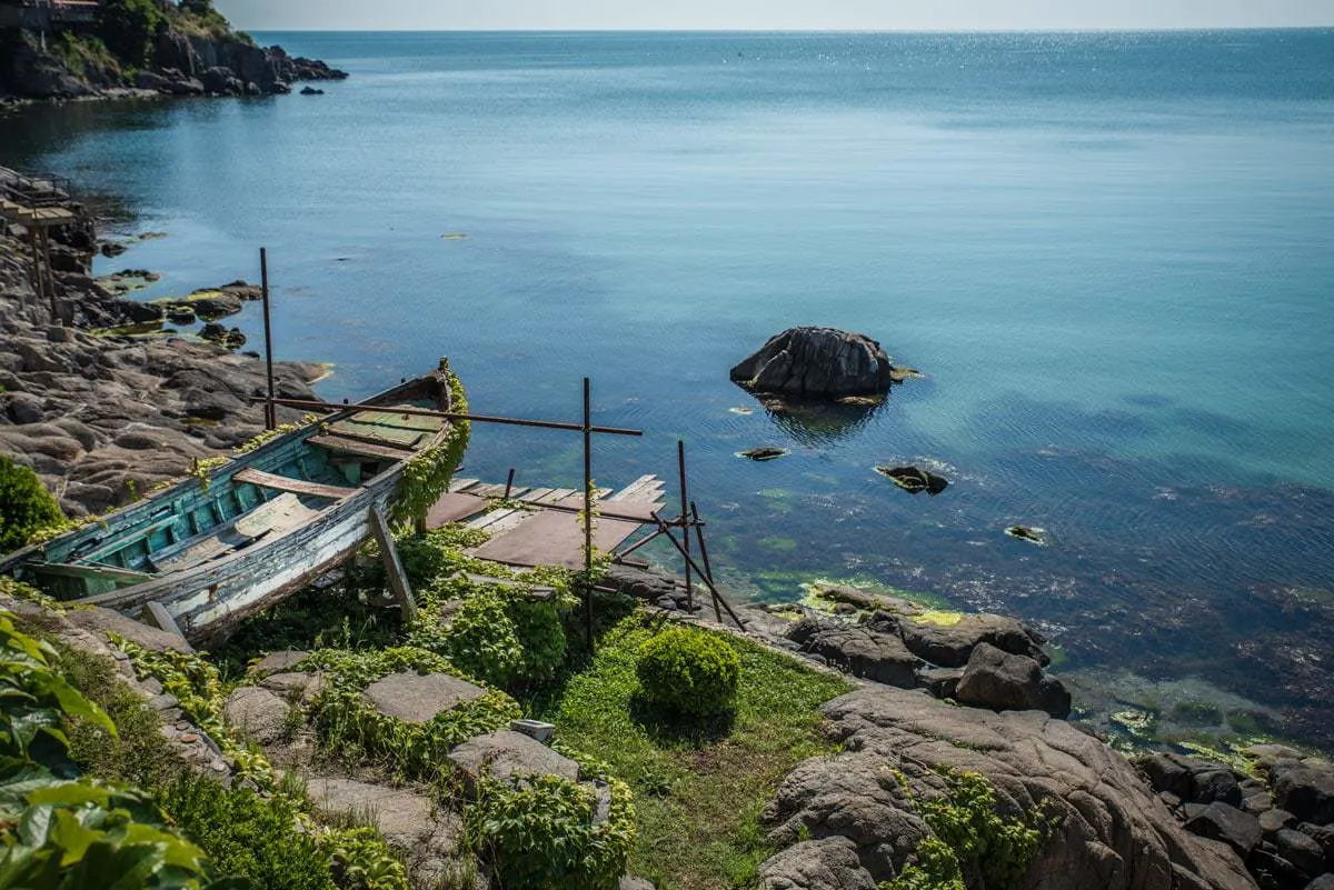 Blue water and rocky coast with a derelict fishing boat in Sozopol Beach.