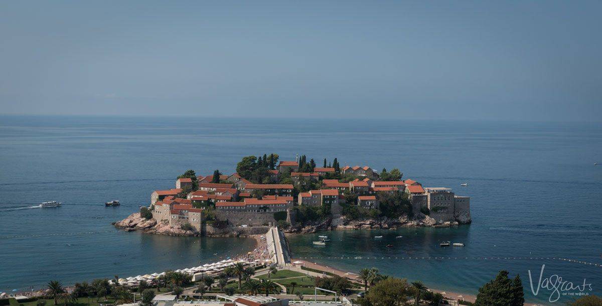 The island of Sveti Stephan in Montenegro with typical red roofs surrounded by blue water and boats. 