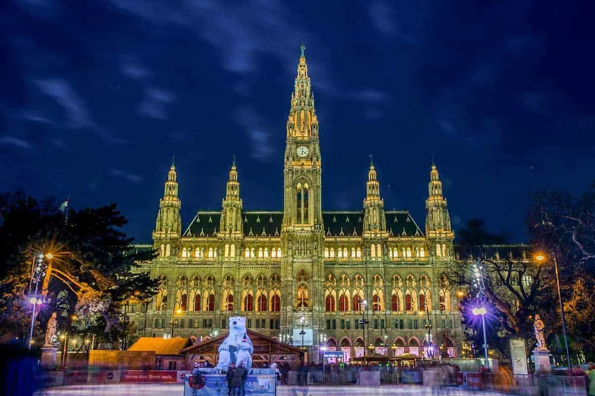 Vienna city hall lit up at night with an ice skating rink in front. 