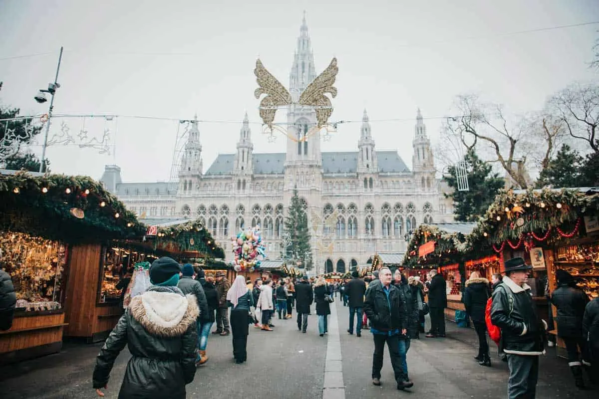 People wandering around Vienna's Christmas markets on a cold day in front of a historical palace. 