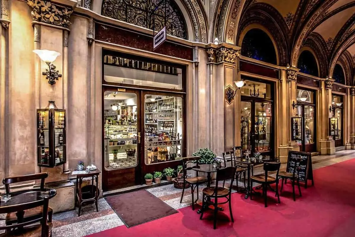 The lit frontage of a traditional Viennese coffee house at night with marble tables under an arcade