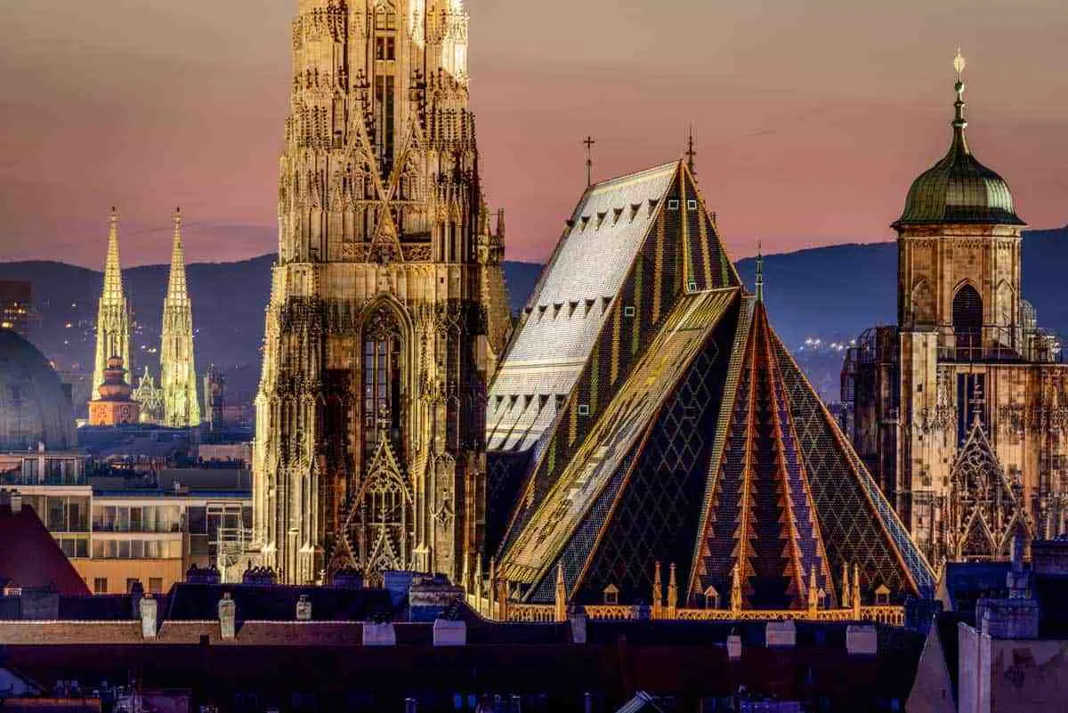 The tiled roof and spires of St Stephen’s Cathedral against a pink dusk sky over the Vienna skyline