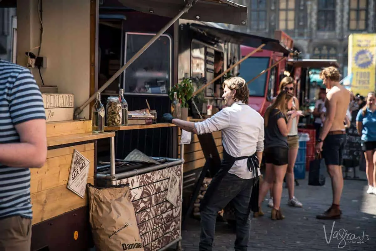 One of the very best free things to do in Ghent - The Barrio Cantina Food Truck Festival with a man standing outside his food truck with people eating delicious street food in the background.