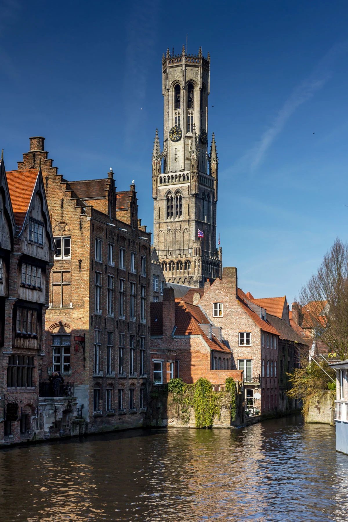 Historic buildings, bell tower on a canal on a sunny day in Bruges. 