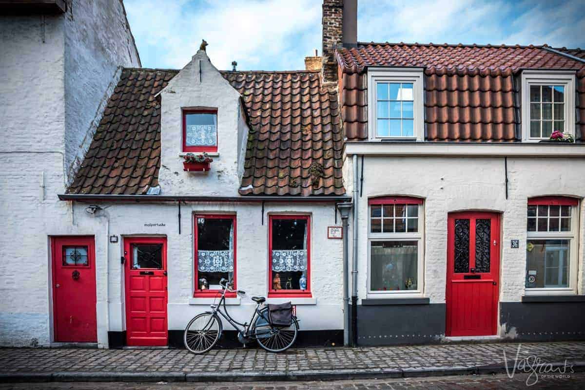 Quaint red brick house with red trim windows and a bicycle out the front in Bruges. 