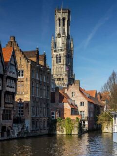 Historic buildings, bell tower on a canal on a sunny day in Bruges.