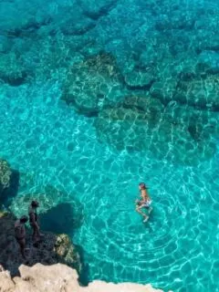 A man swimming in clear blue water beneath cliffs in Cape Greko