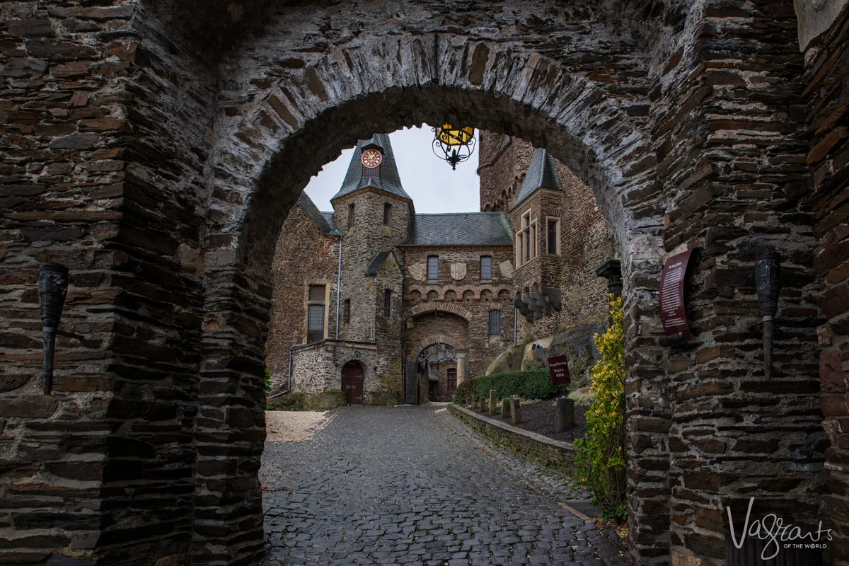 Looking through an arched stone gate into the grounds of a castle in Cochem Germany. 
