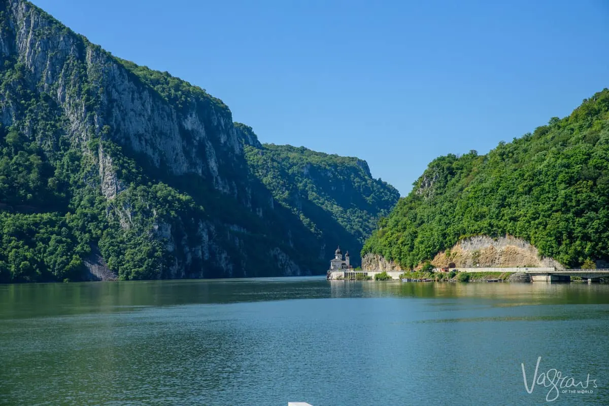 Looking down the Danube river where a onion domed chapel sits in the river bank in between a gorge. 