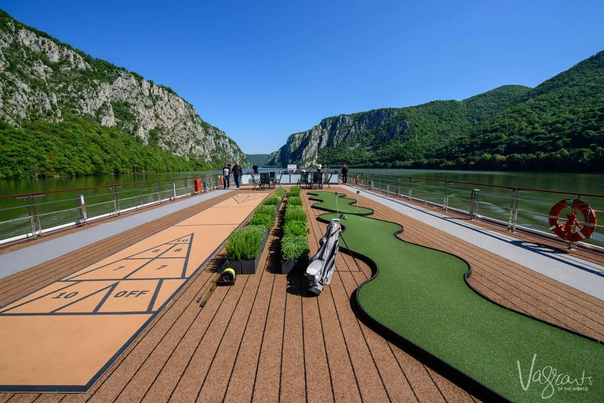 The top deck of a river cruise ship as it sails between a gorge in Romania. There is a mini golf course on the deck. 