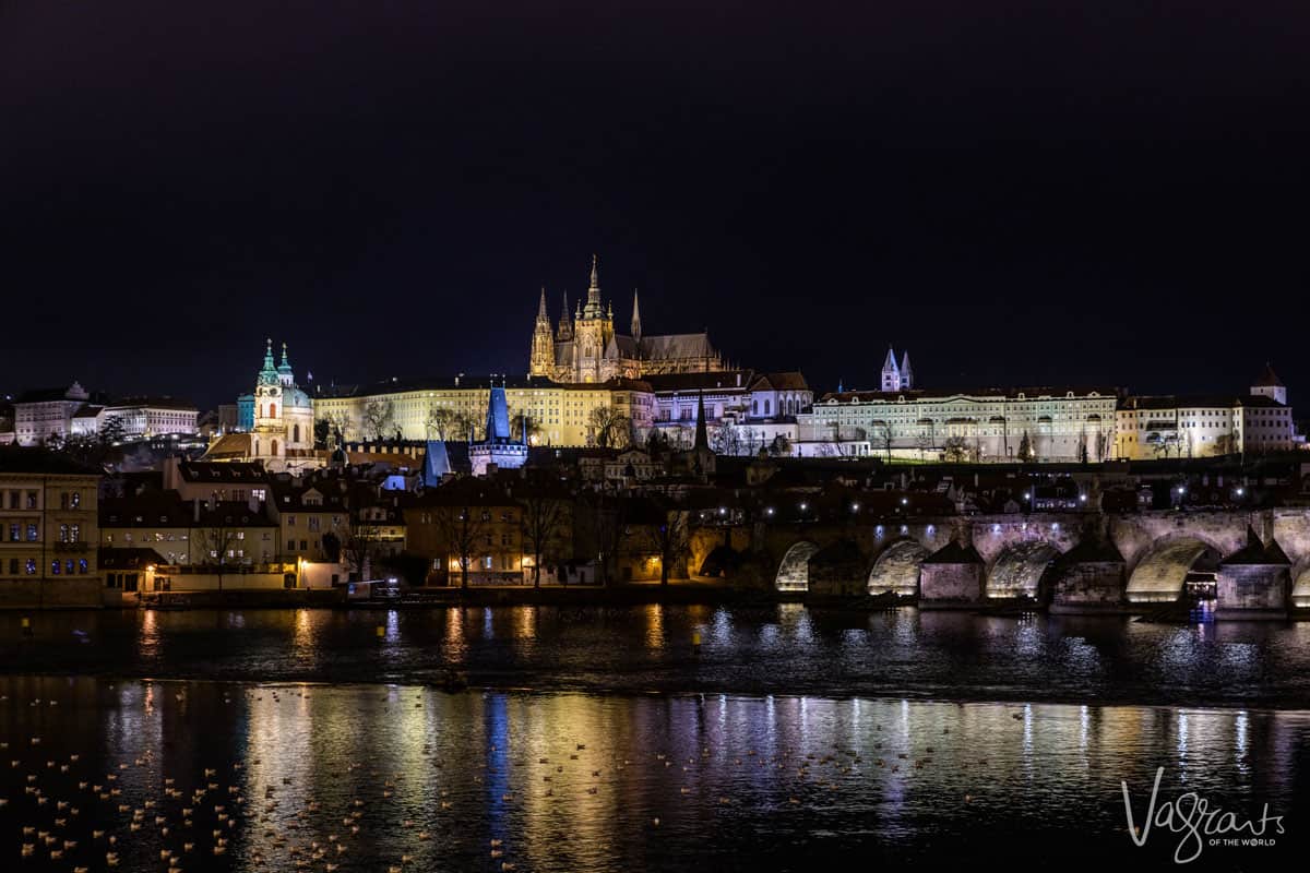 The city of Prague lit up at night with the medieval bridge and castle on the hill. 