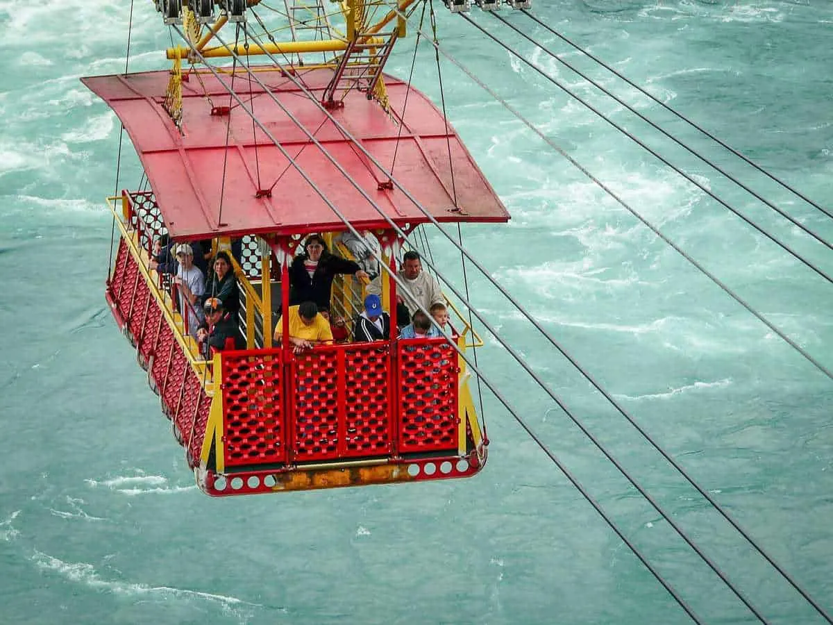 A group of slight scared people in a red Whirlpool Aero Car dangling over the swirling waters of Niagara Falls. A great reason to visit Canada.