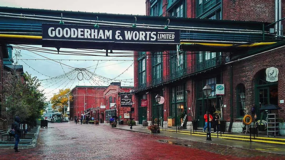 The red cobble stone streets in the Distillery District Toronto with the Gooderham and Worts Distillery sign overhead. It is this style that makes toronto the best places to visit in Canada