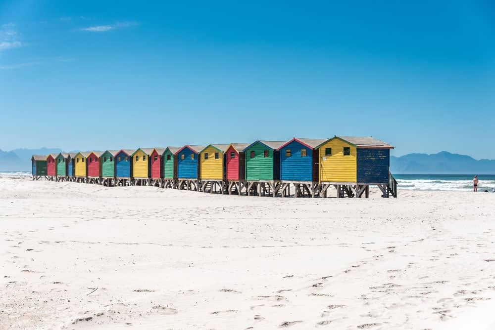 Multi coloured beach huts on white sand in Cape Town. Keep Valuables safe at the beach with a lockable beach bag or beach safe.