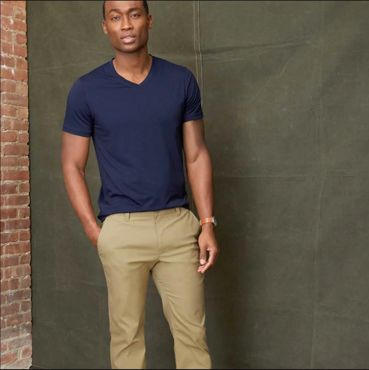 Man standing in front of a kakhi canvas modelling tan chinos and a blue T-shirt. 