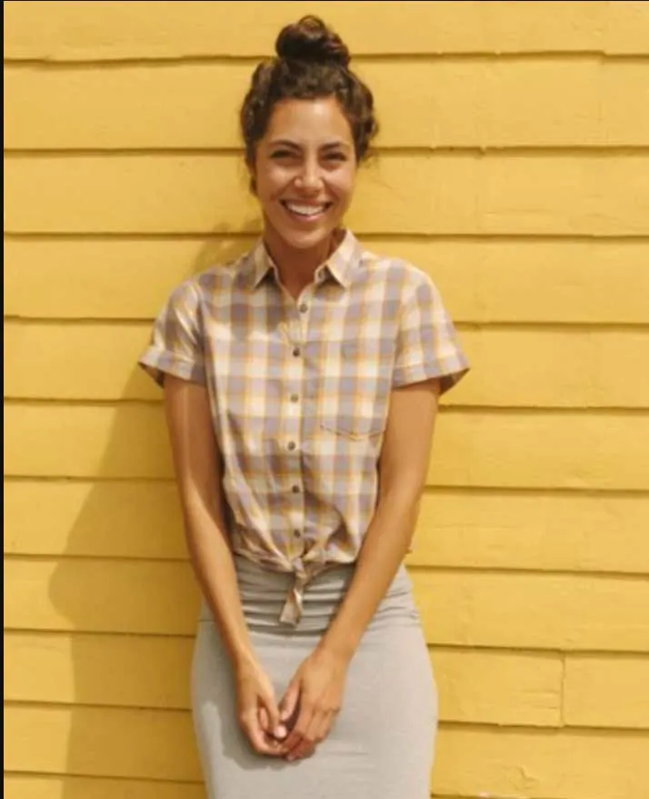 Woman modelling a check shirt leaning against a yellow wall. 