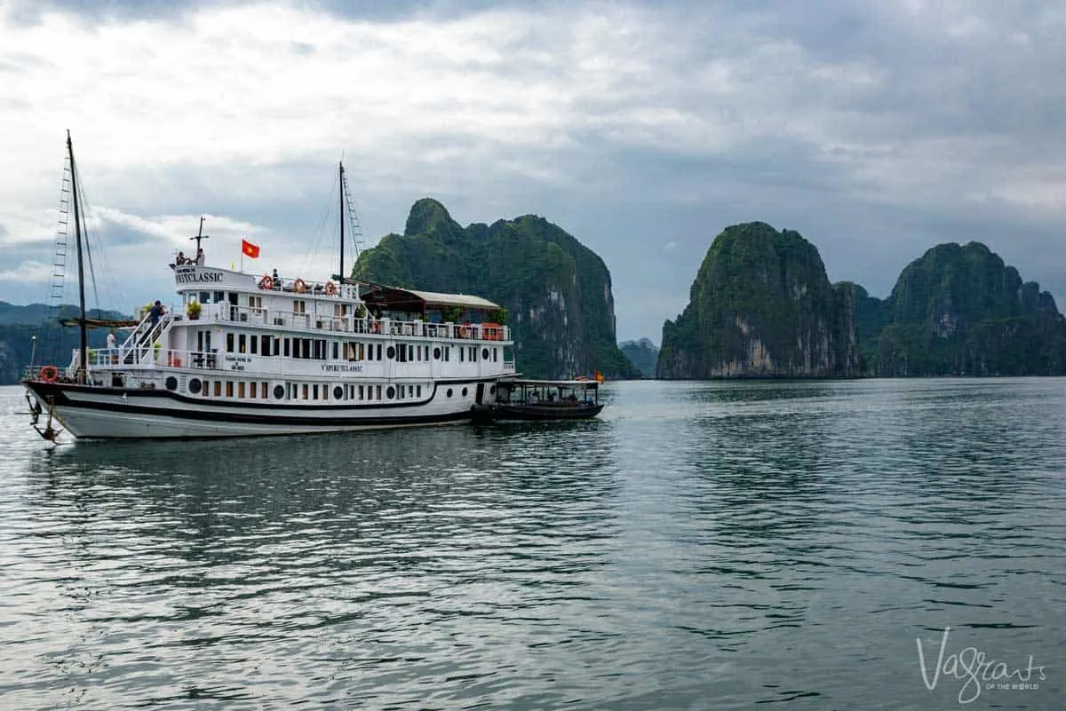 A traditional luxury Junk Boat anchored in a bay with the tall rock Halong islands in the distance. 