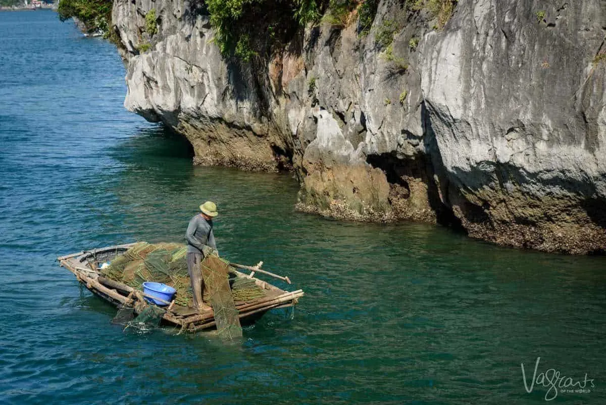 A fisherman sorts nets in a small wooden boat in Halong Bay Vietnam