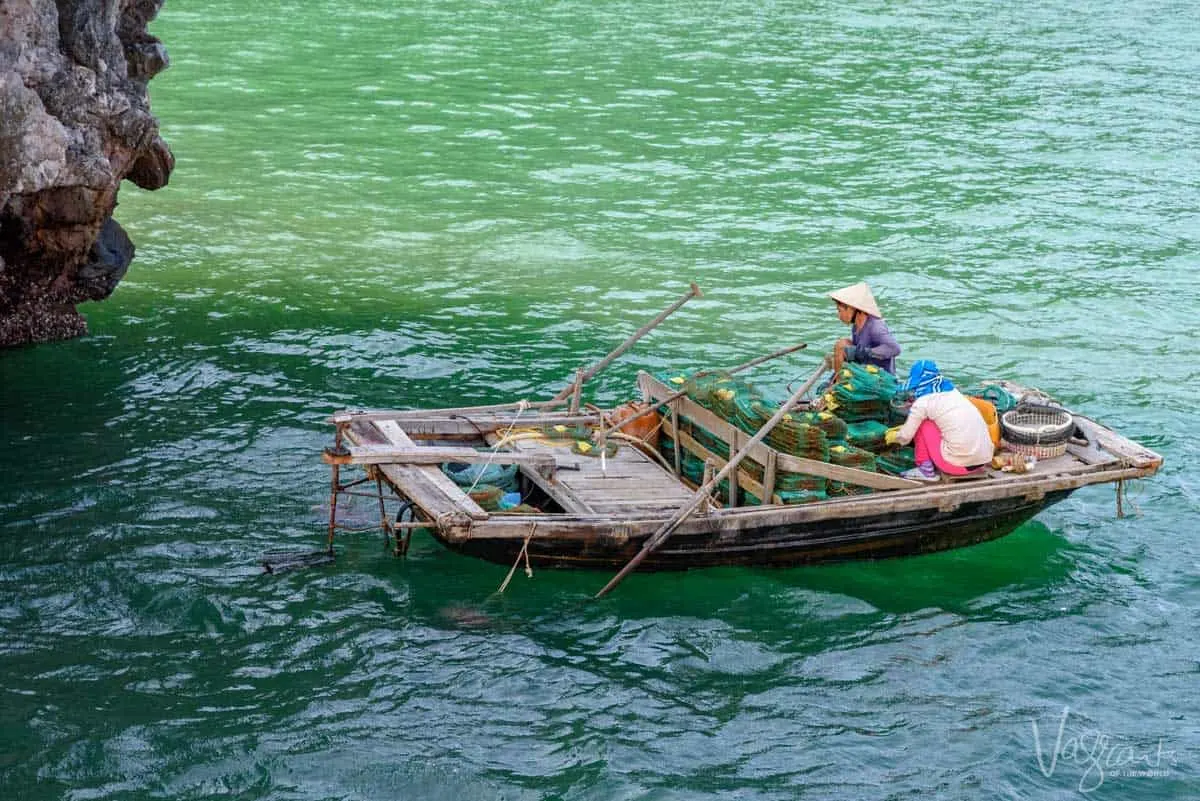 Vietnamese women wearing traditional cone hats in a small wooden fishing boat stacking net traps. 