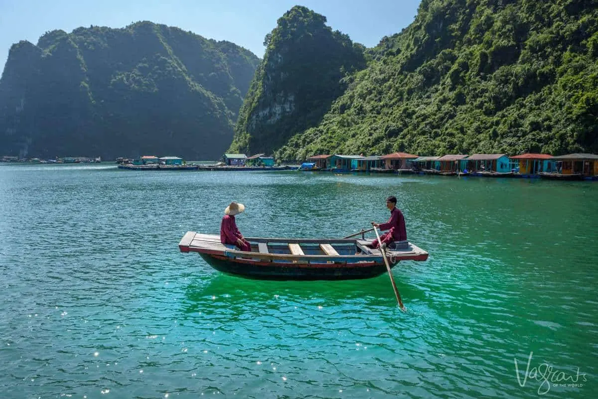 Local men in a row boat in Halong Bay with floating fishing huts in the distance. 