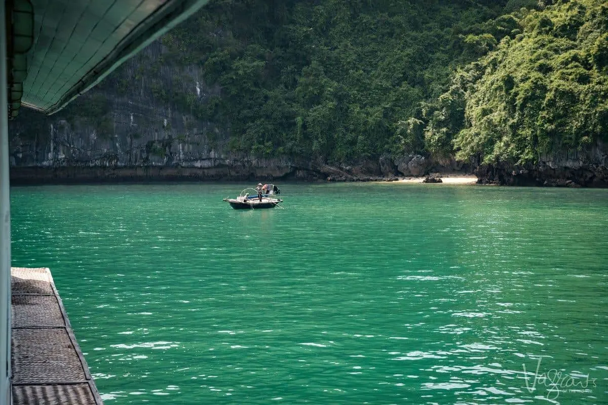 A traditional Vietnamese fisherman throws nets from a small wooden boat in a clam bay. 