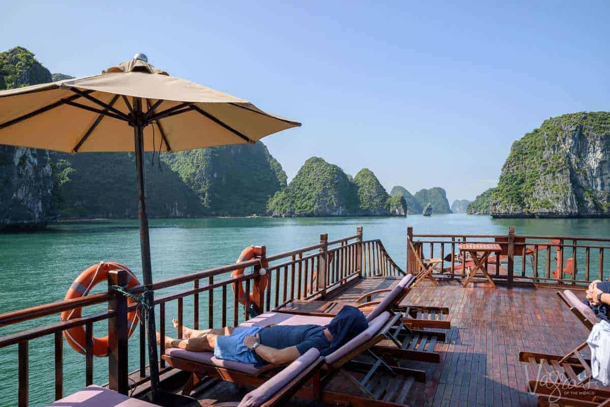A man lies on a sun lounge on the deck of a luxury Halong Bay Junk Boat. 