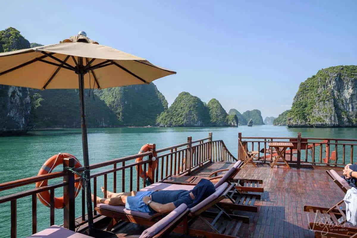 A man lies on a sun lounge on the deck of a luxury Halong Bay Junk Boat. 