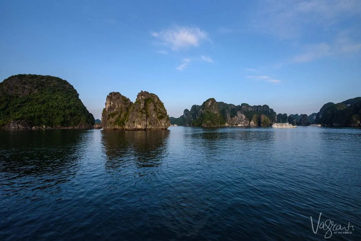 A luxury Halong Bay Junk Boat Cruises past the rocky island in the bay on a clear morning. 