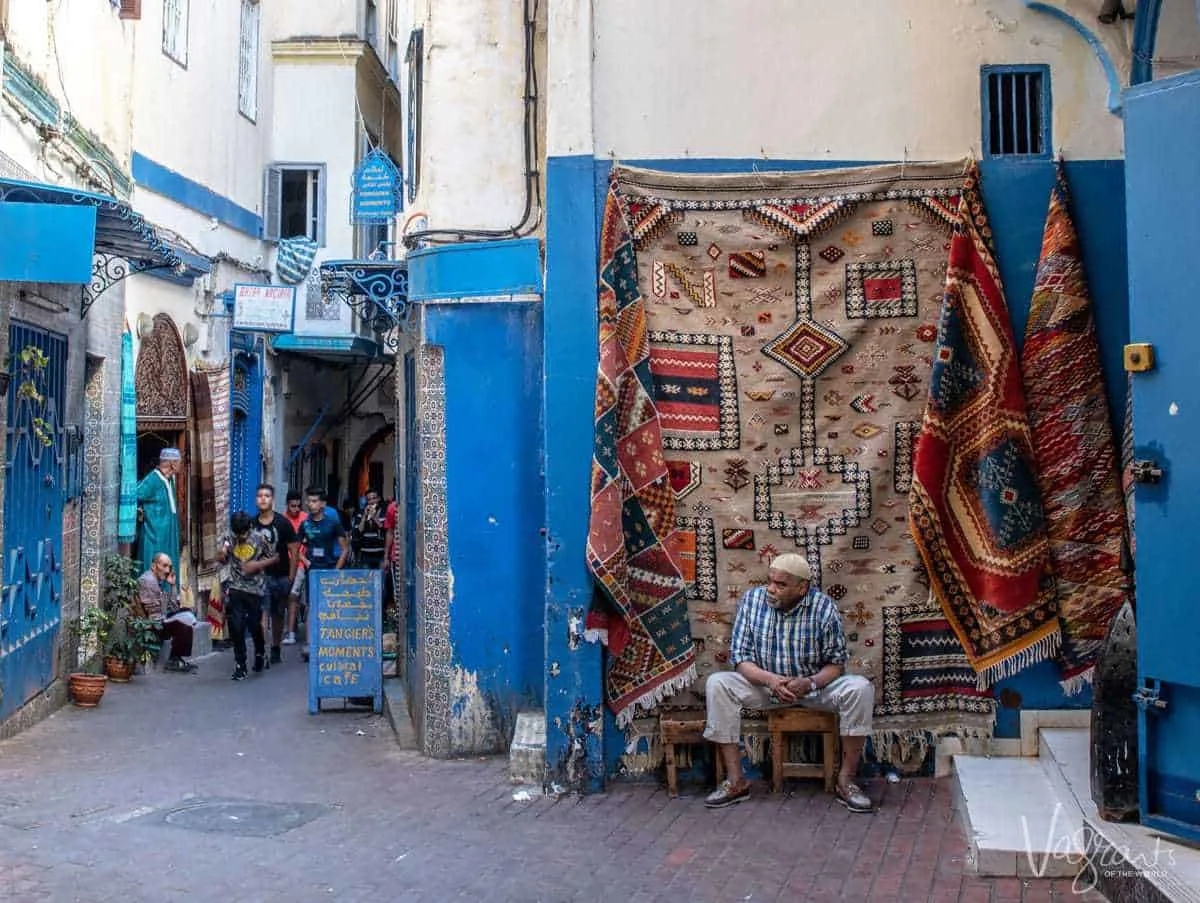 Moroccan man sitting in front of hanging carpets in the medina in Tangier Morocco.